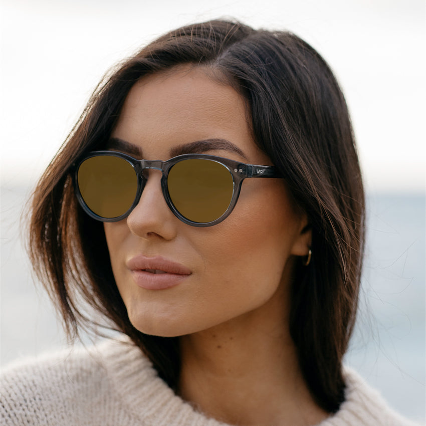 Woman wearing stylish round sunglasses with a notched keyhole bridge and double rivet details on frame sides
