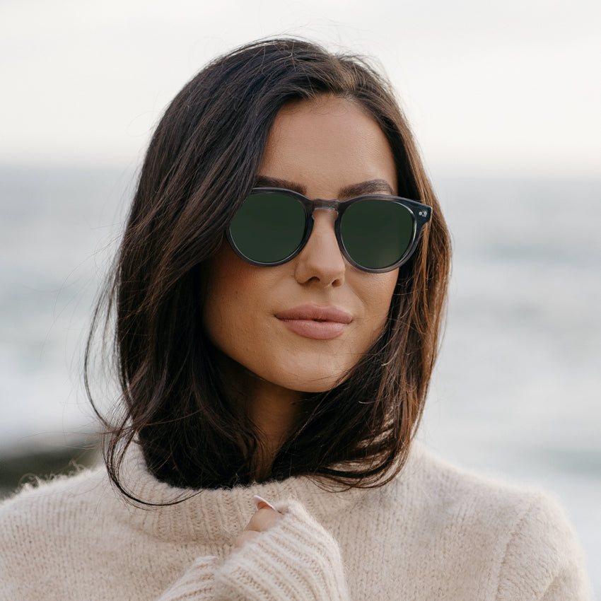 Woman wearing retro round-shaped sunglasses with a notched keyhole bridge and double rivets by the ocean
