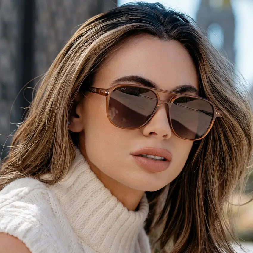 Woman wearing oversized square aviator sunglasses with rounded edges and brown lenses in outdoor setting