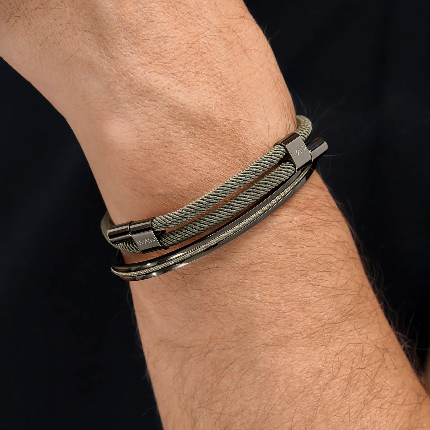 Olive Green / Gunmetal || Olive green rope bracelet with polished gunmetal clasp paired with slim metal bangle on wrist against black background