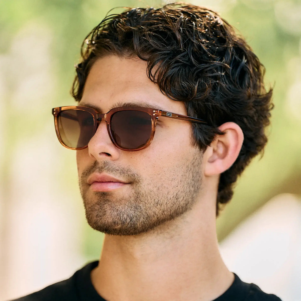 Crystal Brown / Amber || Square prescription sunglasses with crystal brown acetate frame and amber lenses worn by man with curly hair outdoors