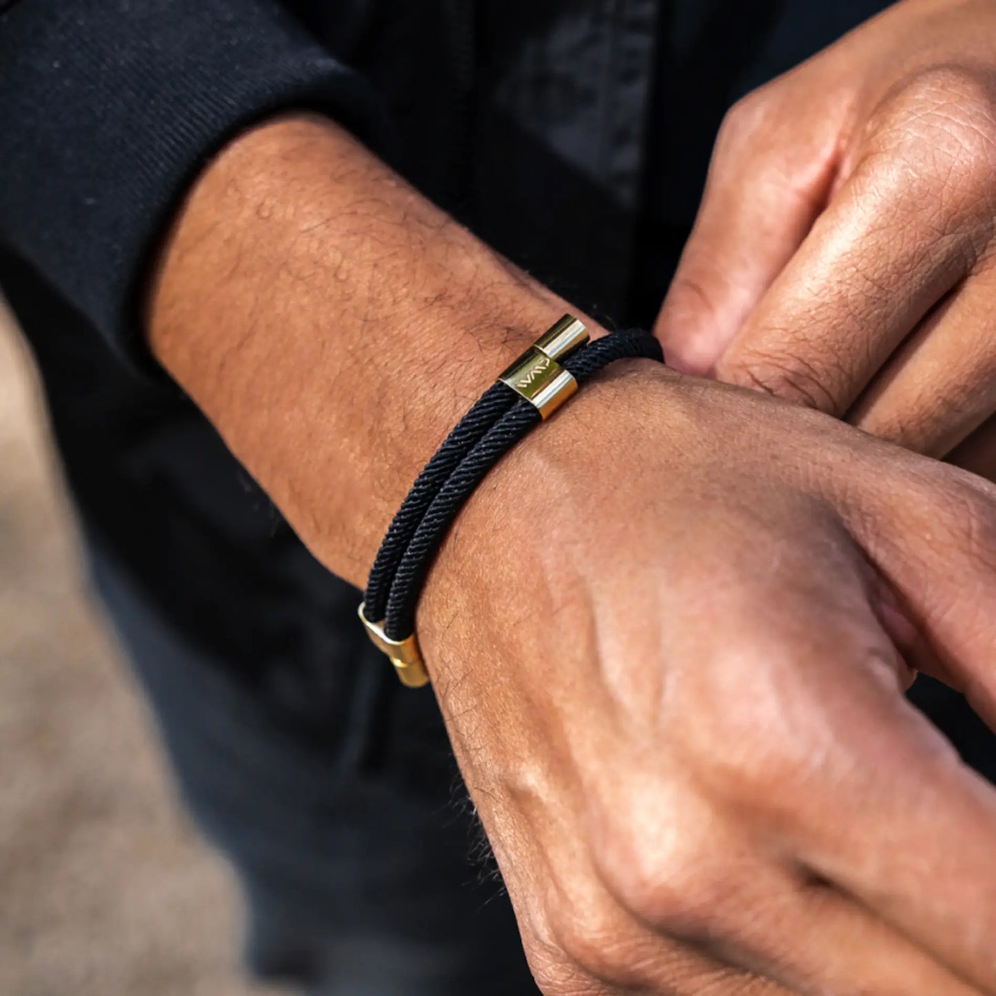 Onyx Black / Gold || Black twisted rope bracelet featuring polished gold clasp worn on wrist with dark clothing background