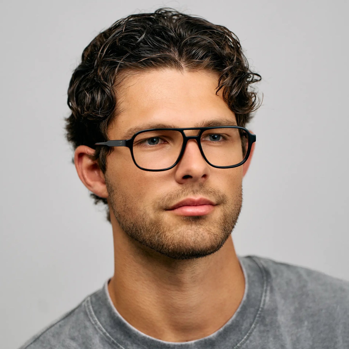 Black || Blue light glasses with bold black aviator frames worn by man with dark curly hair against light background