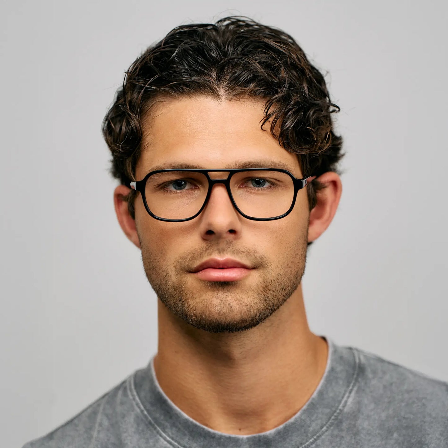 Black || Blue light glasses with bold black aviator frames worn by man with dark curly hair against plain grey background