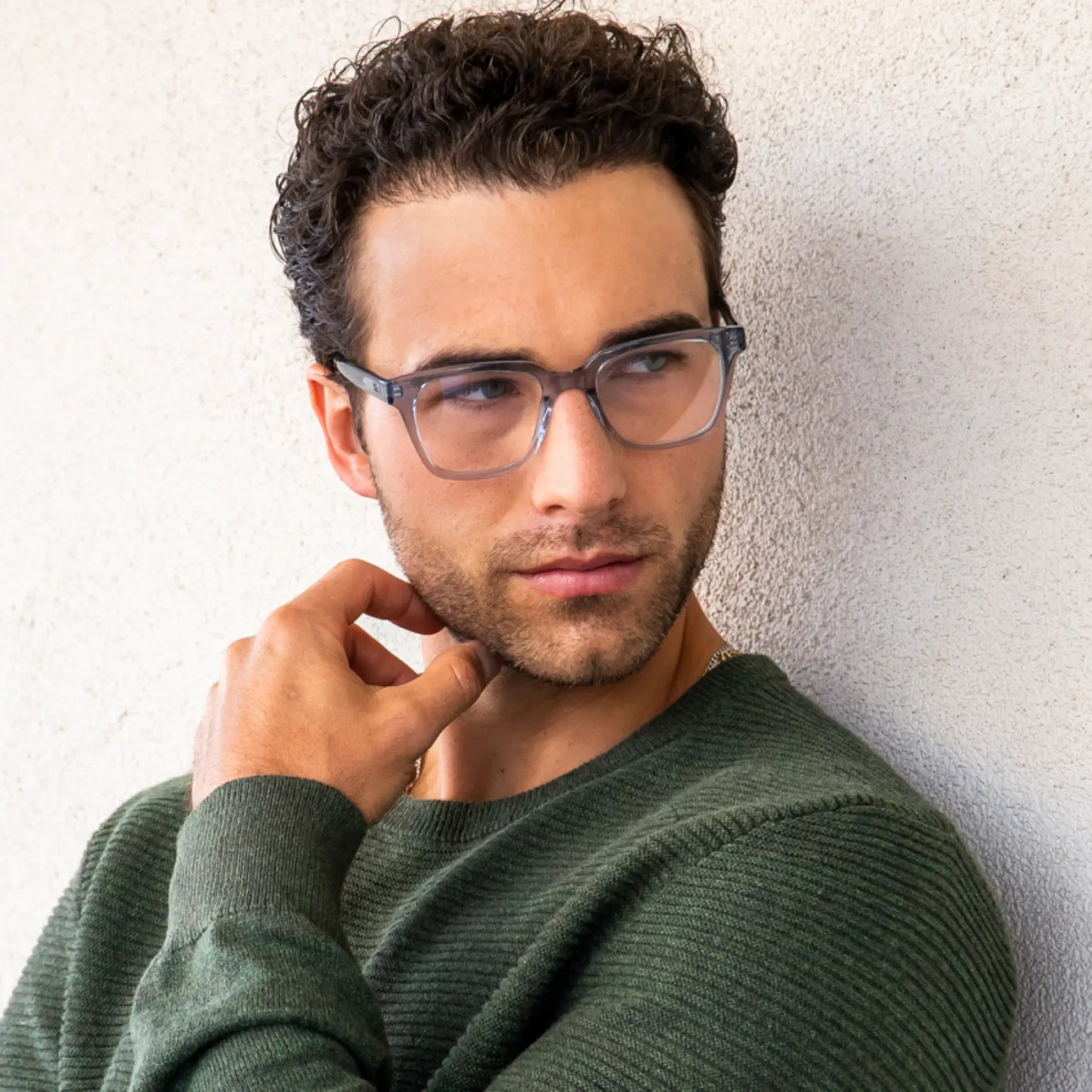 Denim Blue || Carson translucent blue square frame glasses worn by man in green sweater leaning on textured beige wall