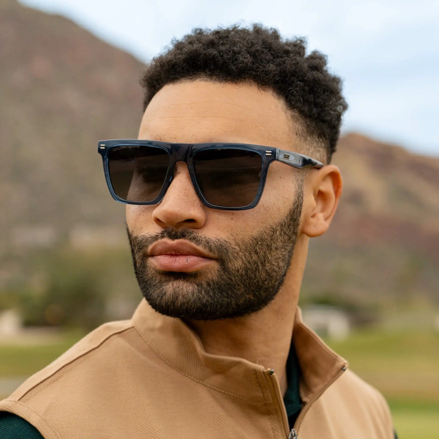 Man wearing stylish dark performance sunglasses outdoors with blurred mountain landscape background