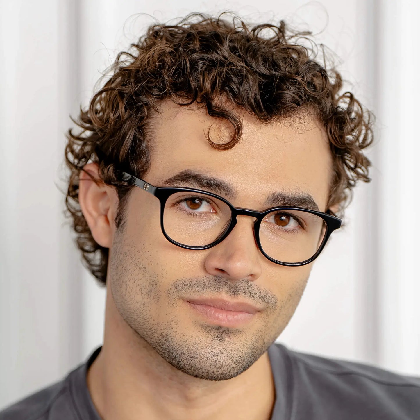 Black || Square prescription glasses with thin black acetate frame and keyhole bridge worn by man with curly hair indoors in natural light