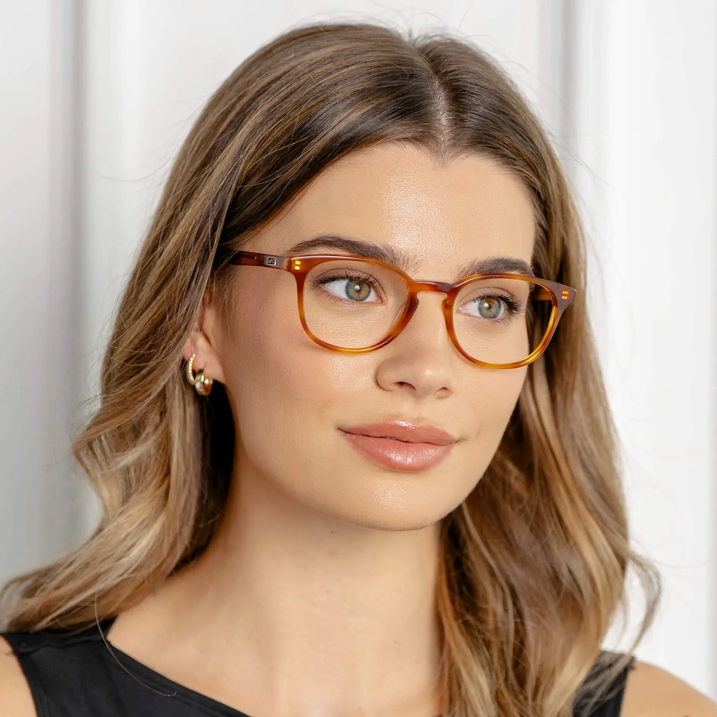 Honey Tortoise || Miles blue light glasses with translucent honey tortoise round frames worn by woman with wavy hair in soft lighting