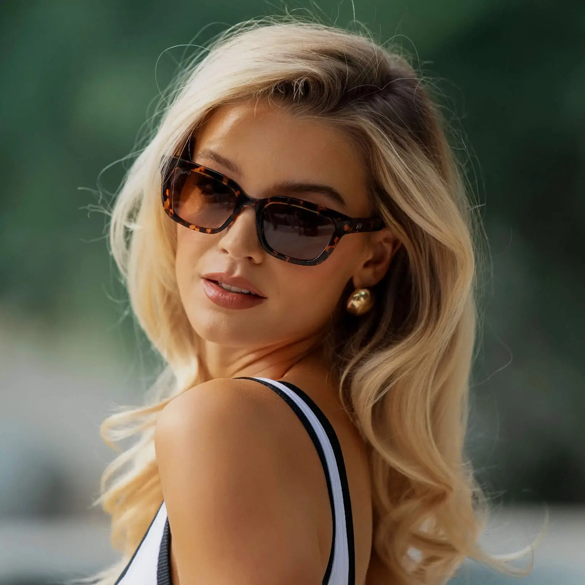 Ember Tortoise / Amber || Rectangular sunglasses with thick acetate tortoiseshell frames and dark lenses featuring a straight bridge worn by a women outdoors