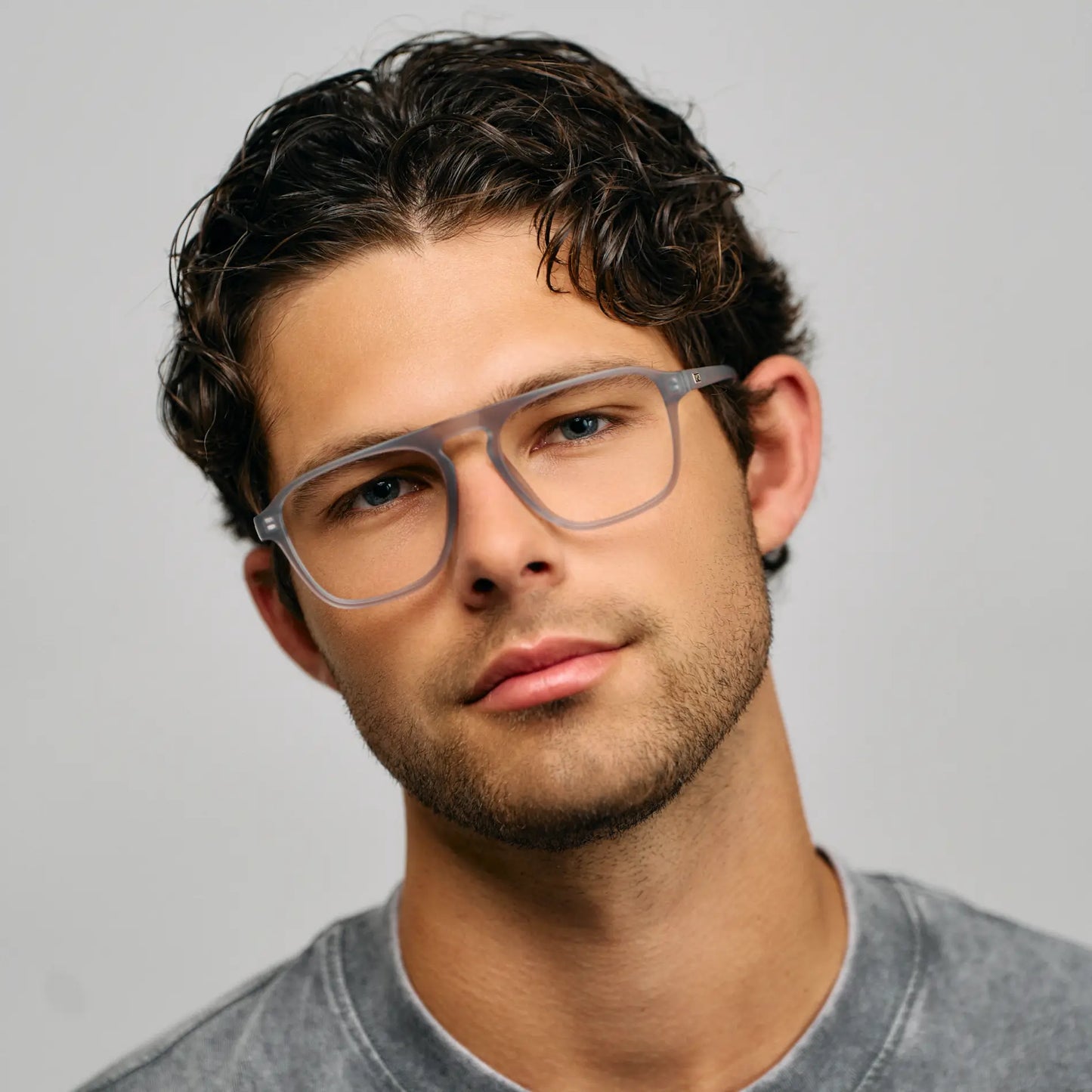 Close-up of man wearing lightweight rectangular aviator acetate eyeglasses with a single bridge against gray background