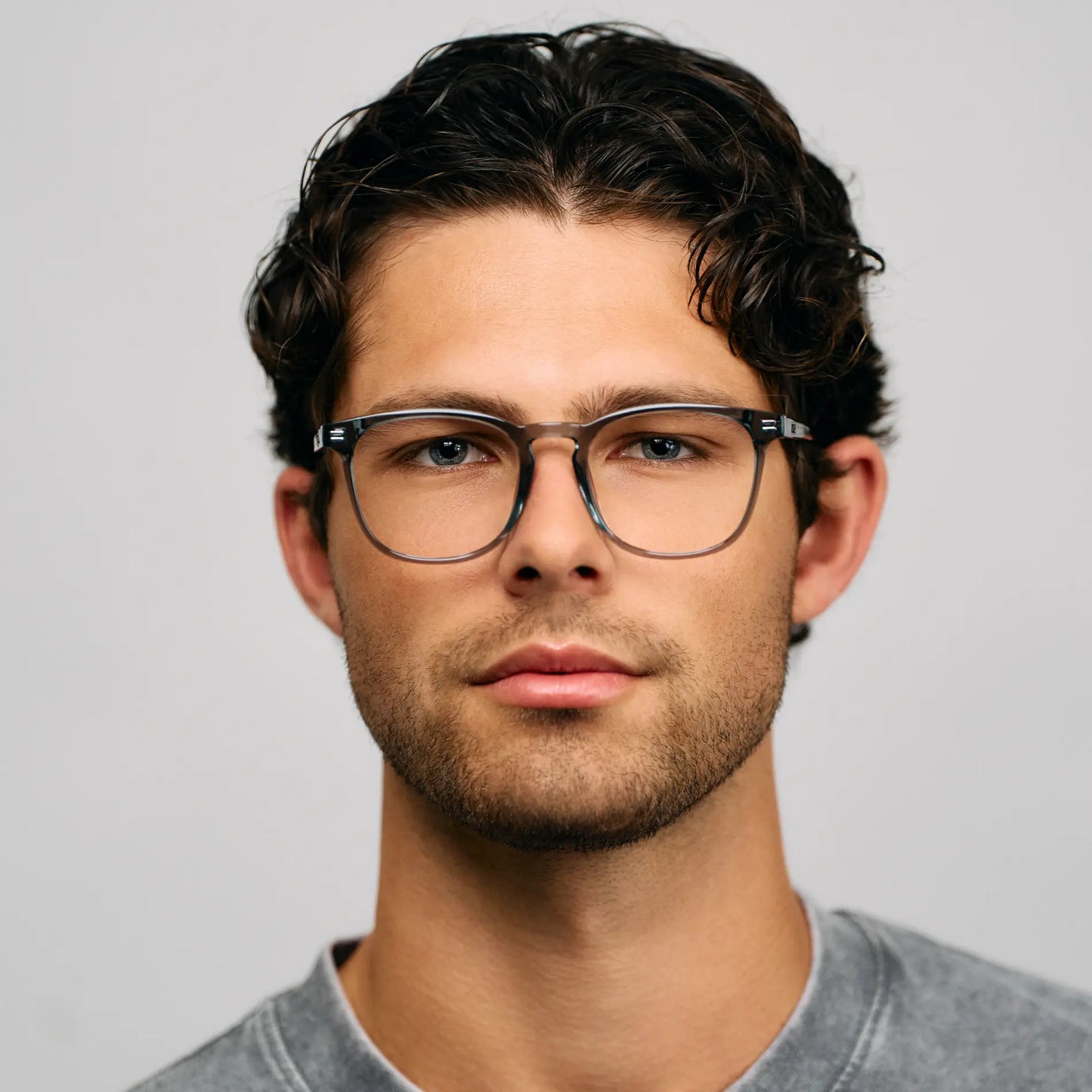 Crystal Stone Blue || Square prescription glasses with crystal stone blue acetate frame and bridge worn by man with curly hair against plain gray background