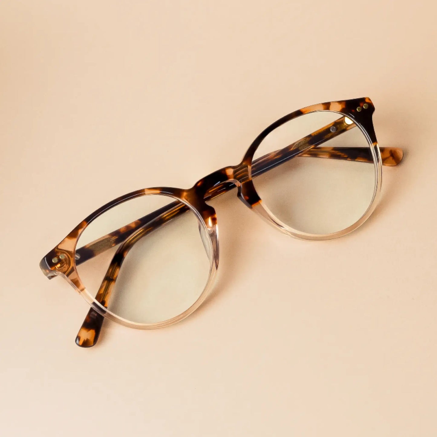 Crystal Brown Tortoise || Owen blue light glasses with semi-transparent tortoise shell round frame resting on beige background