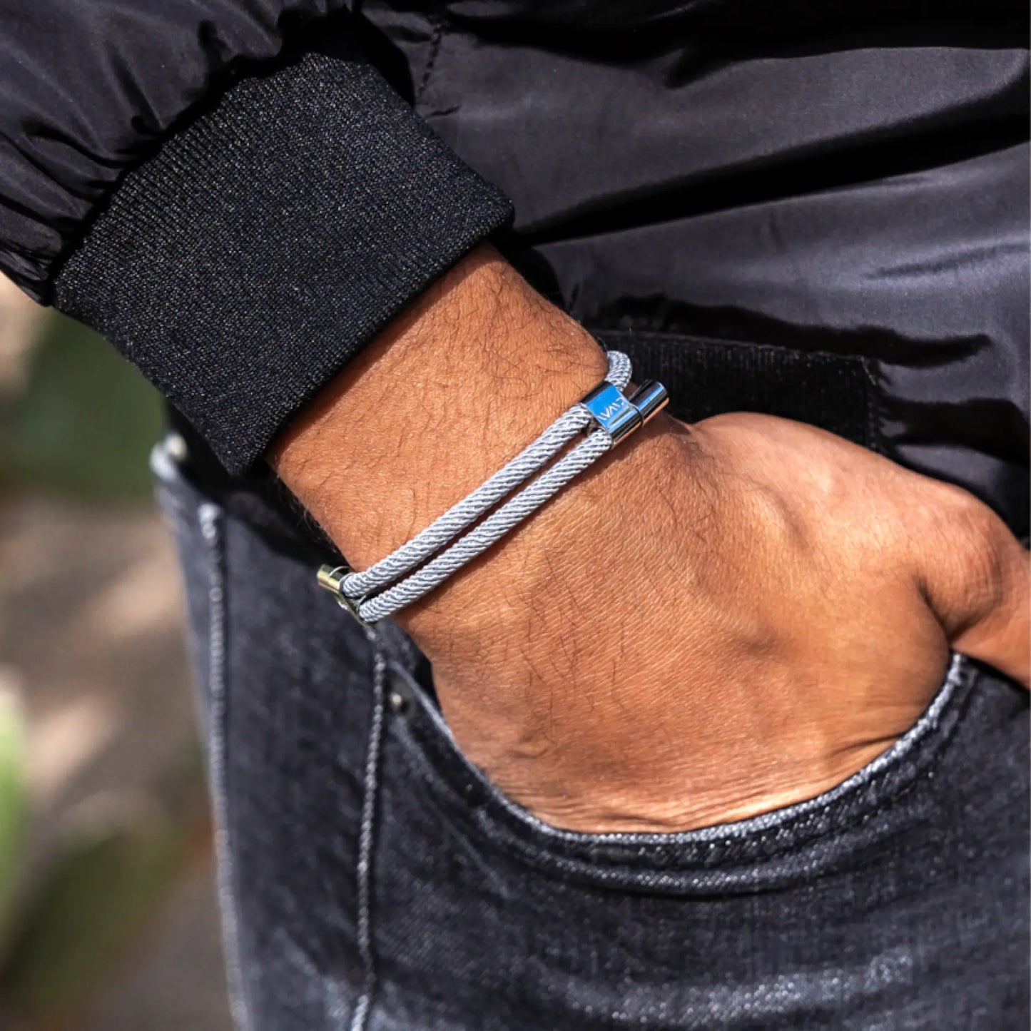 Stone Grey / Silver || Light grey twisted cord bracelet with blue accent bead worn on wrist over casual black and denim outfit