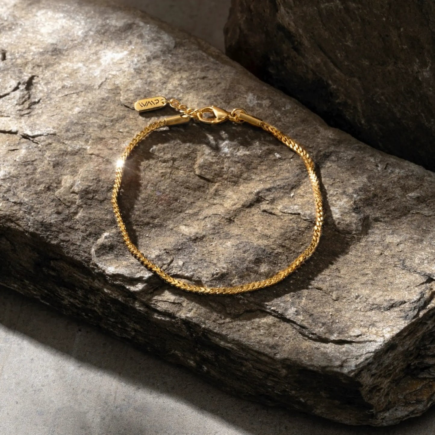 Gold || Gold chain bracelet with lobster clasp resting on textured stone surface in natural light