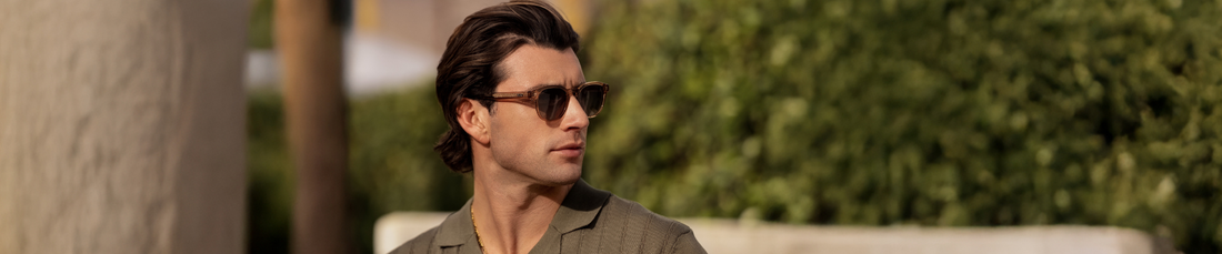 Man wearing sunglasses outdoors, looking to the side with greenery in the background