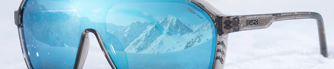 Close up of Ryder sunglasses with mirror blue lenses resting on snow with mountains reflected in the lenses