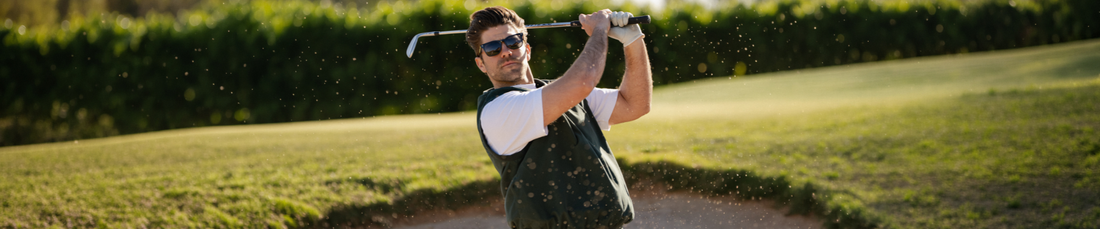 Man swinging a golf club outdoors wearing a white tee shirt and sunglasses