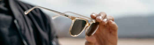 Close up of hand holding a pair of beige translucent sunglasses outdoors in natural light