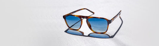 Single pair of aviator sunglasses with classic tortoiseshell acetate frames and gradient blue lenses, displayed on a light textured surface in natural sunlight