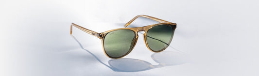 Single pair of round sunglasses with translucent warm beige acetate frames and flat green lenses, displayed at an angle on a white surface with soft natural shadows