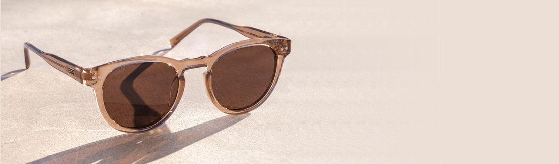 Pair of sunglasses with brown frame and lens resting on a light surface in natural light