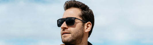 Man looking sideways wearing sunglasses outdoors against a blue sky