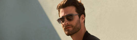 Man wearing sunglasses standing against a sunlit wall.