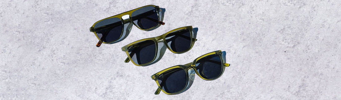 Three pairs of low bridge, green frame sunglasses arranged on a textured light surface