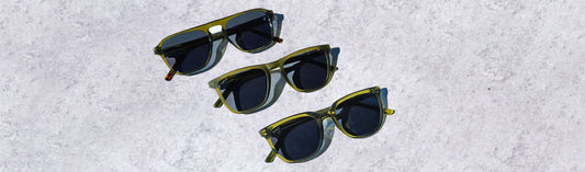 Three pairs of low bridge, green frame sunglasses arranged on a textured light surface