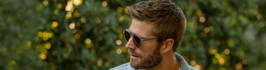 Man wearing stylish sunglasses outdoors, looking to the side with a blurred green background