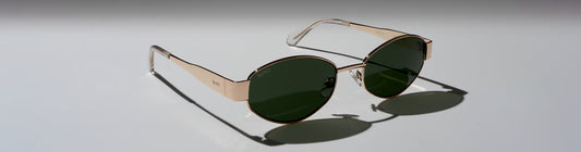 Close up of Verona sunglasses with green lenses and a gold frame displayed on a light background.
