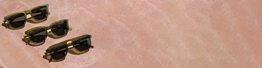 Flat lay of three pairs of sunglasses on a warm-toned textured background