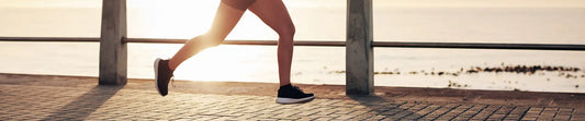 Close up of a person running along a waterfront path at sunrise, showing only their legs and running shoes.
