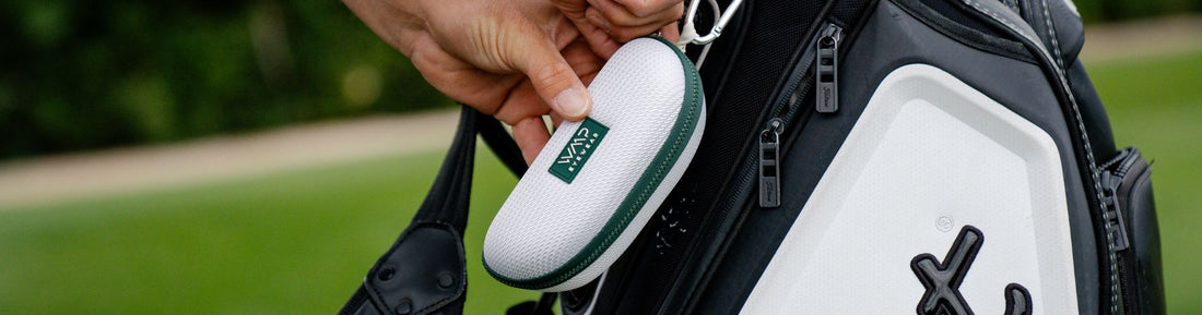 Hand holding a Fairway sunglasses case beside a golf bag in an outdoor setting