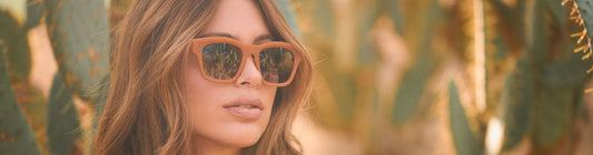 Woman wearing oversized orange frame sunglasses outdoors with cactus plants in the background