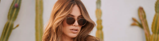 Woman wearing sunglasses in natural light outdoors with cactus plants in the background.