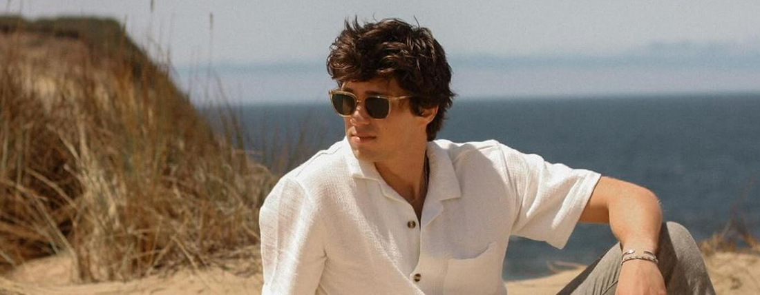Man wearing sunglasses sitting outdoors near the coast with the ocean in the background