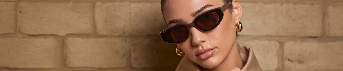 Model wearing WMP Eyewear Astra sunglasses in Mocha Brown with brown lenses, featuring an angular cat-eye frame.