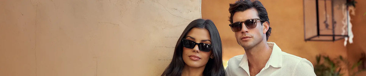 Man and woman wearing sunglasses against a warm tan backdrop.