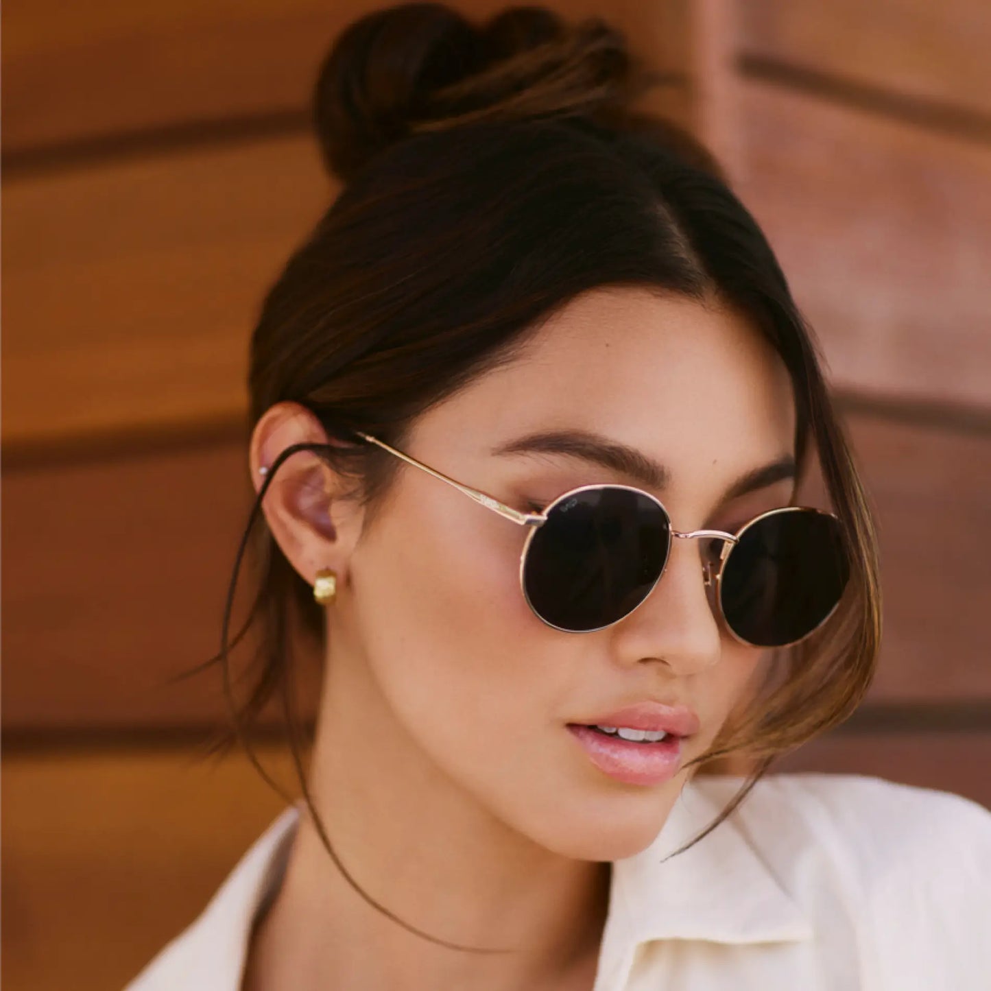 Brown Case || Woman wearing gold frame round sunglasses with dark lenses against wooden background