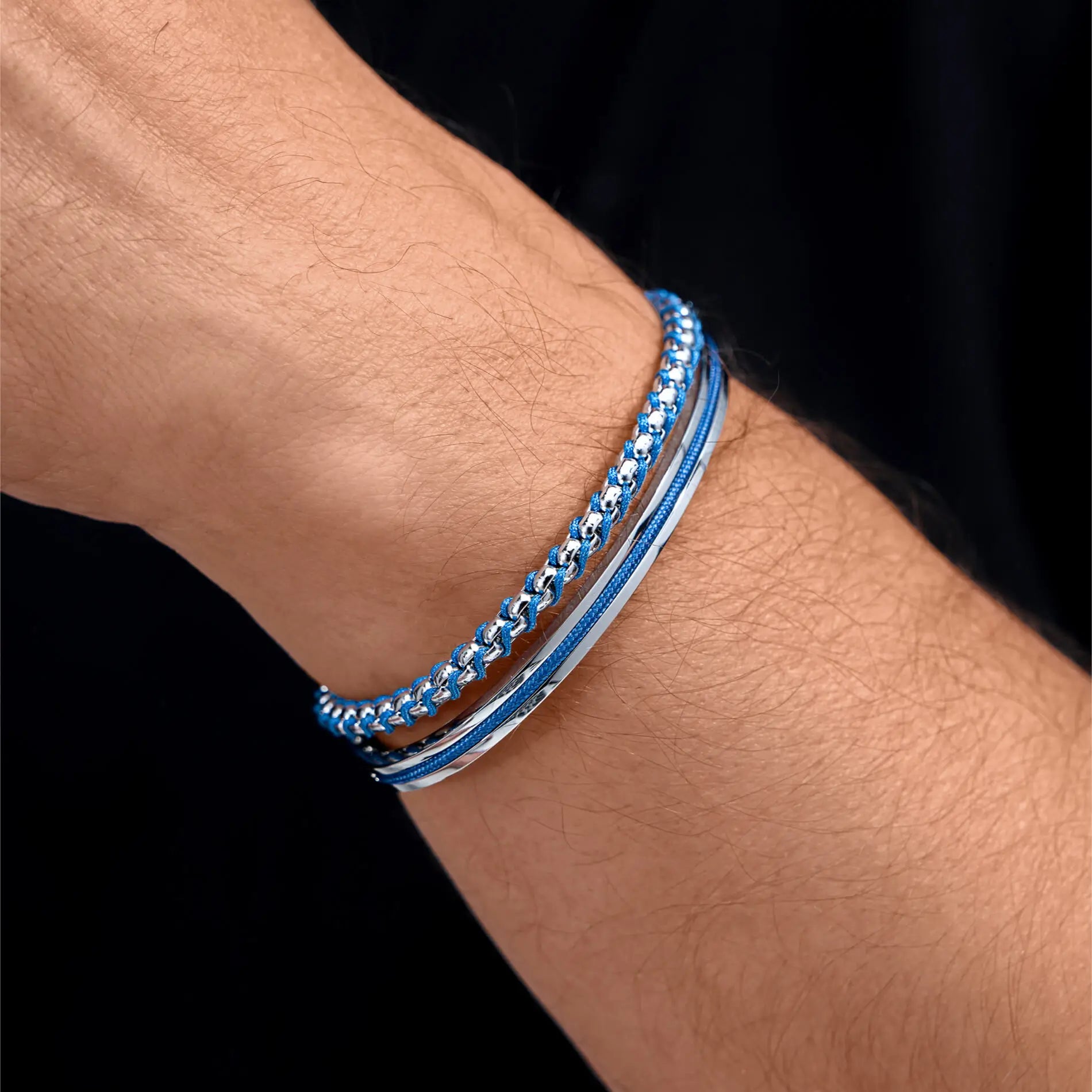Silver / Blue || Close up of wrist wearing a layered silver and blue bracelet set with chain and solid band details on black background