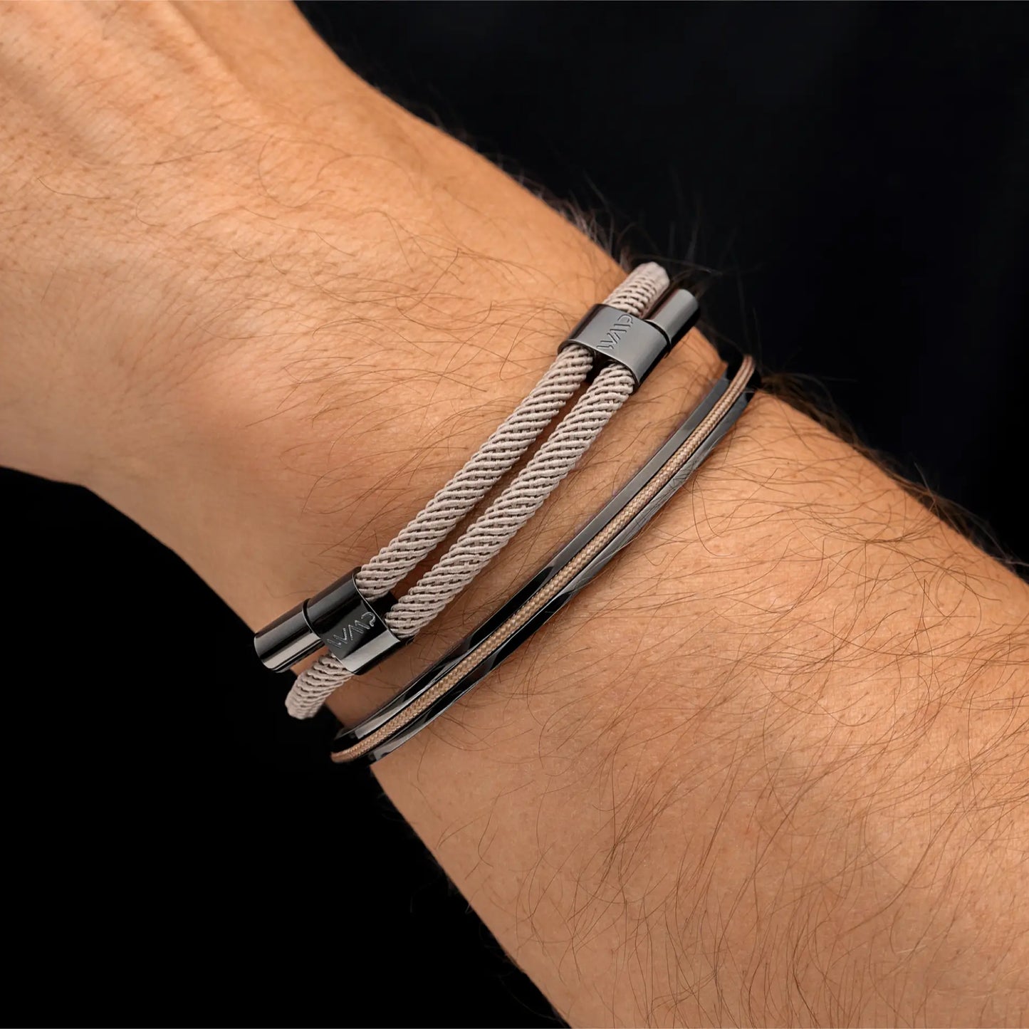 Sand / Gunmetal || Light beige double cord bracelet with dark metallic clasp paired with slim matching bangle on wrist against black background