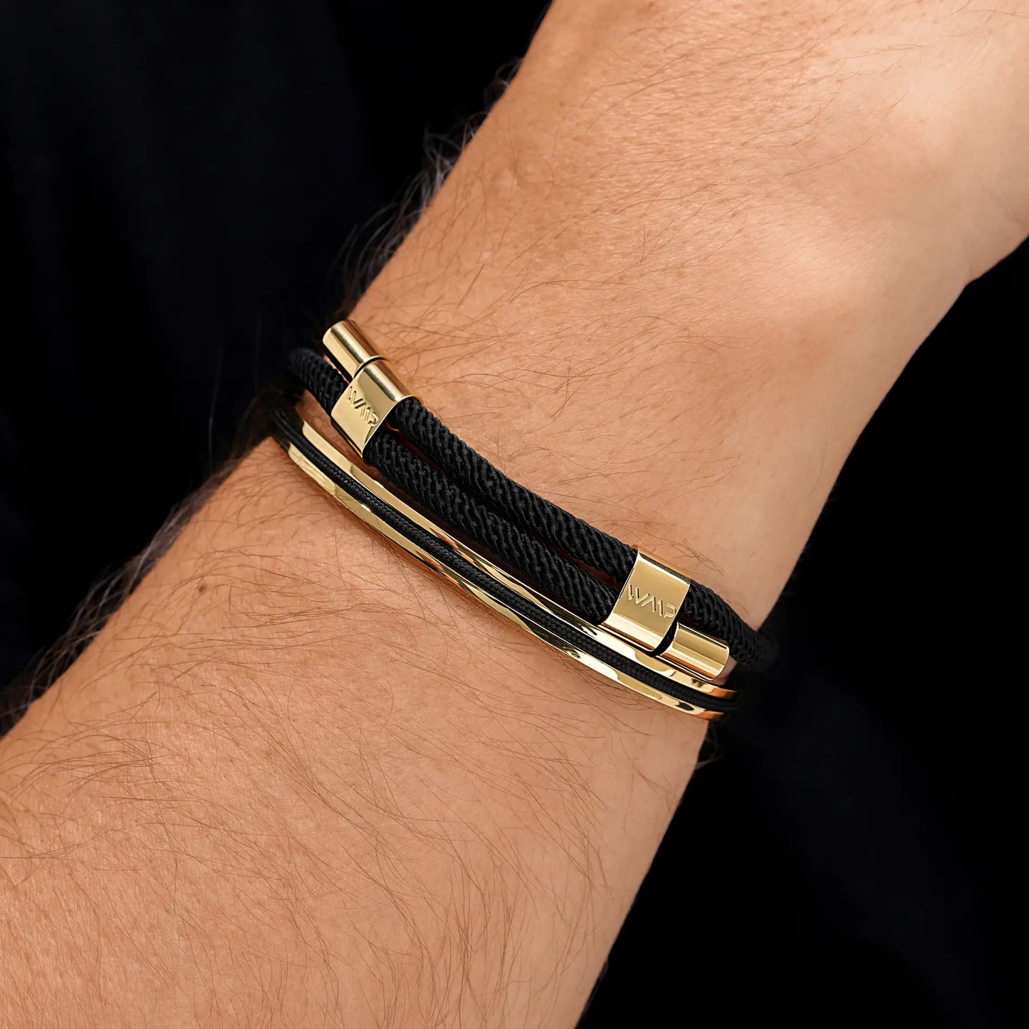 Onyx Black / Gold || Black woven cord bracelet with polished gold bars worn on wrist against dark background