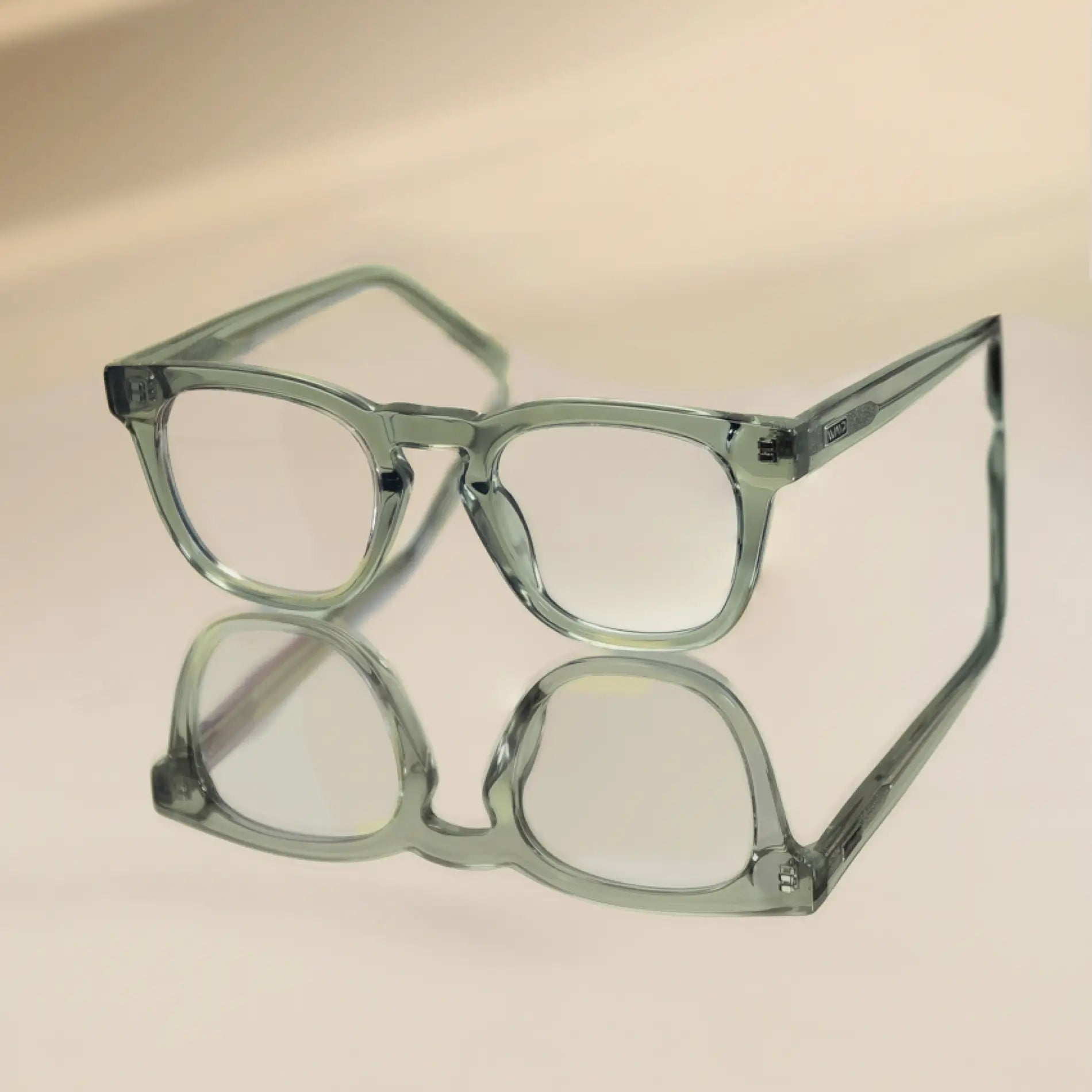 Sea Salt Grey || Square modern prescription eyeglasses with transparent sea salt grey frame resting on reflective surface