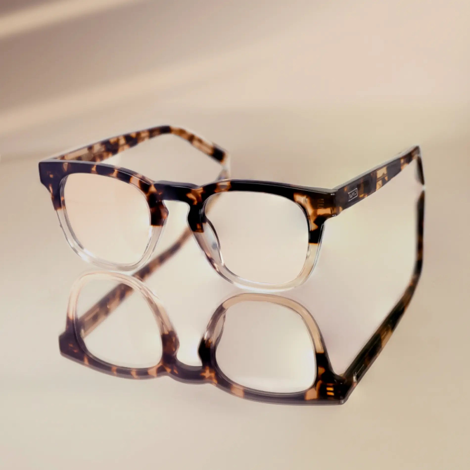 Crystal Brown Tortoise || Square modern prescription eyeglasses with transparent brown tortoise frame resting on reflective surface