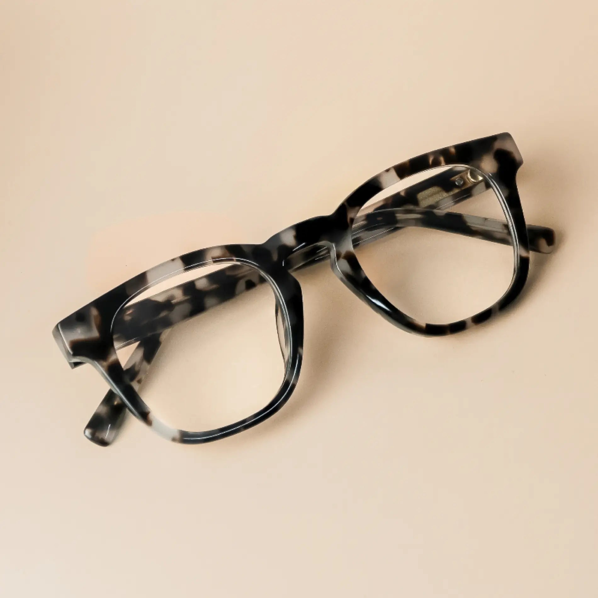 Stone Grey Tortoise || Black and beige tortoise acetate rectangular frame glasses with clear lenses on smooth beige surface