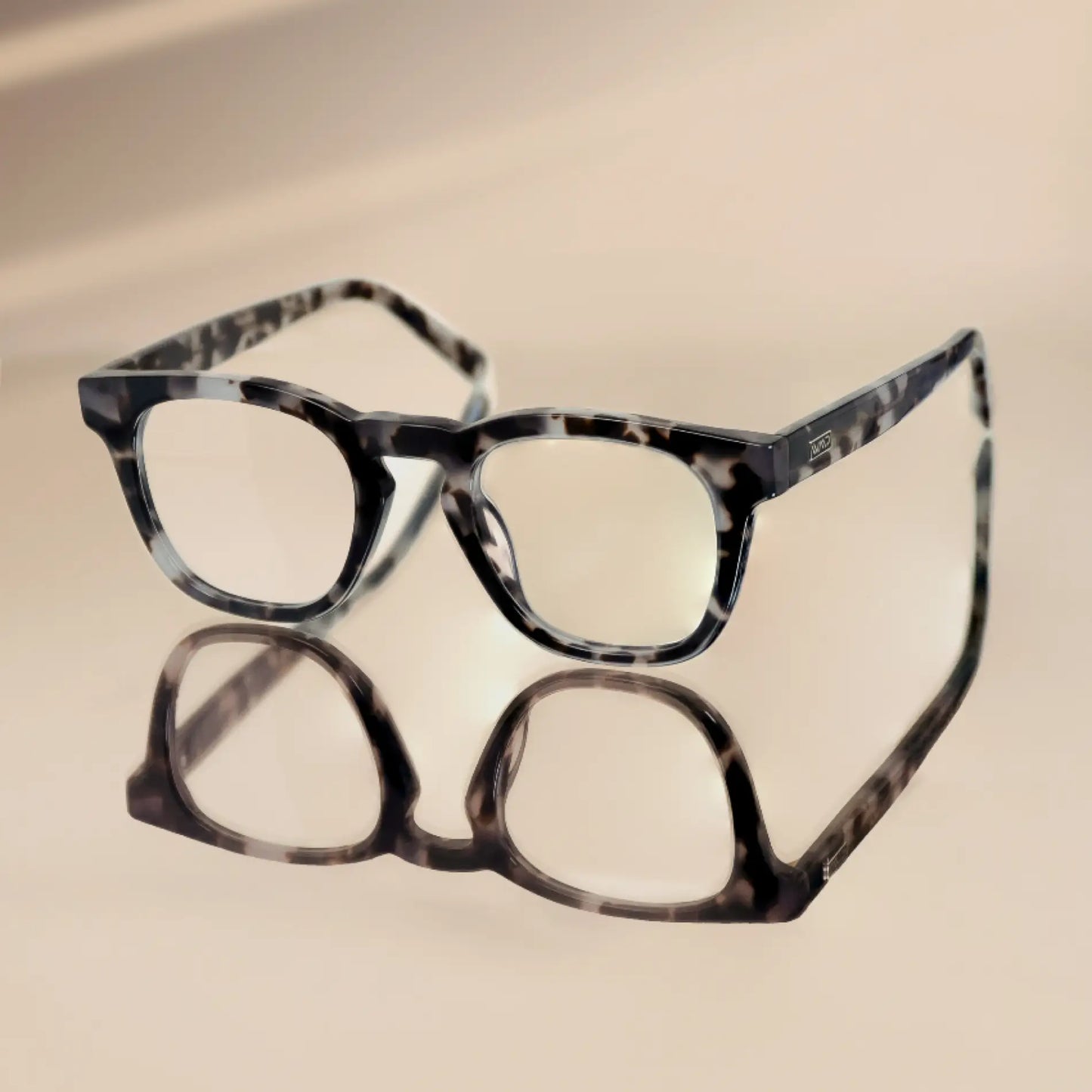 Stone Grey Tortoise || Square modern prescription eyeglasses with transparent stone grey tortoise frame resting on reflective surface