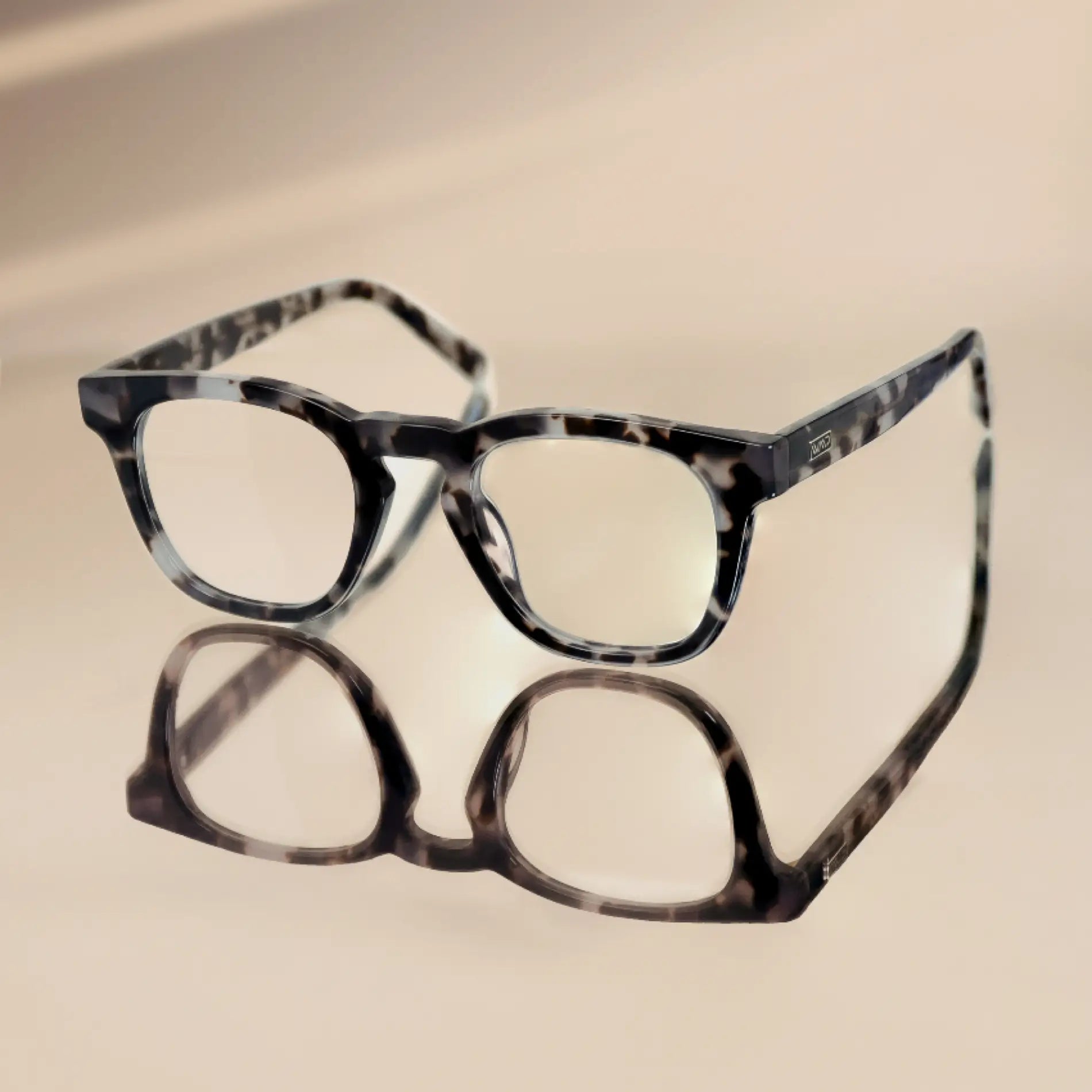 Stone Grey Tortoise || Square modern prescription eyeglasses with transparent stone grey tortoise frame resting on reflective surface