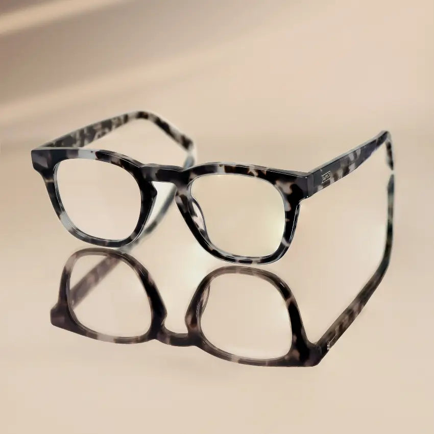 Stone Grey Tortoise || Tortoiseshell round frame glasses with clear lenses reflecting on smooth beige surface