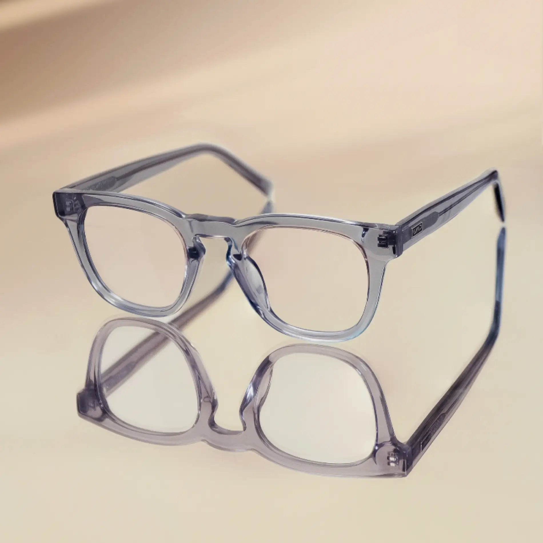 Crystal Lilac Grey || Translucent blue square frame blue light glasses resting on reflective surface with soft beige background